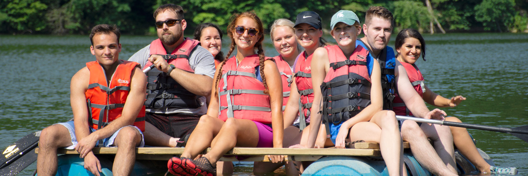 A group of students sit on a raft on the water.