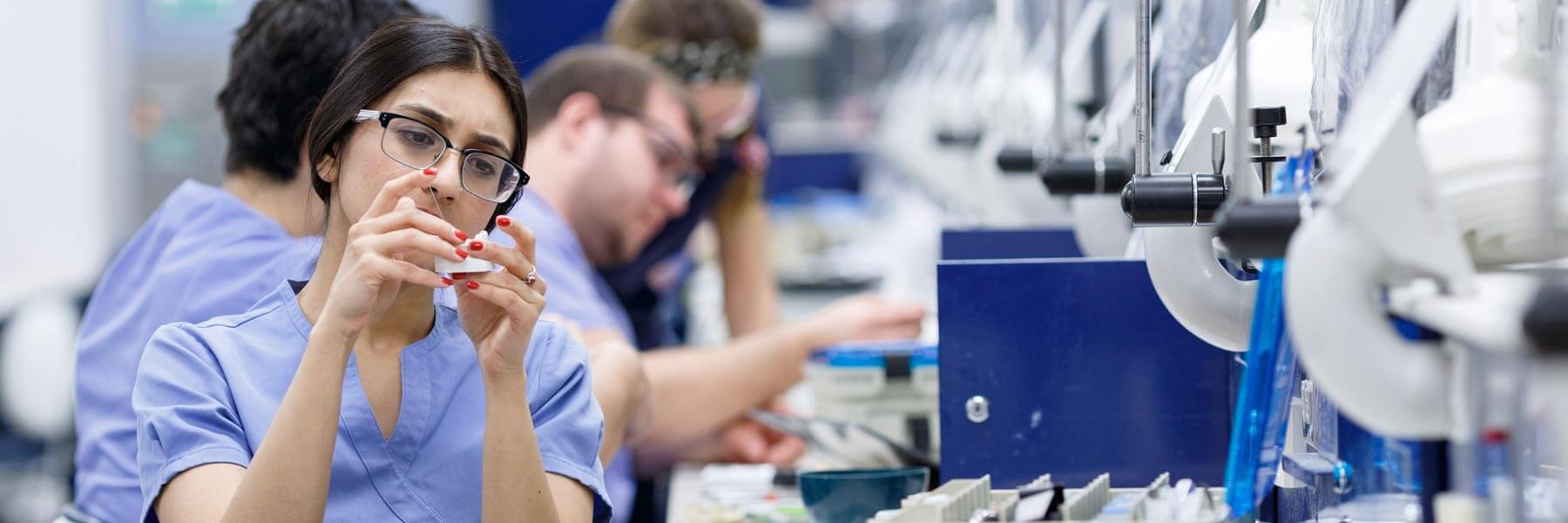 A dentistry student wears protective glasses and works with tools in a lab.