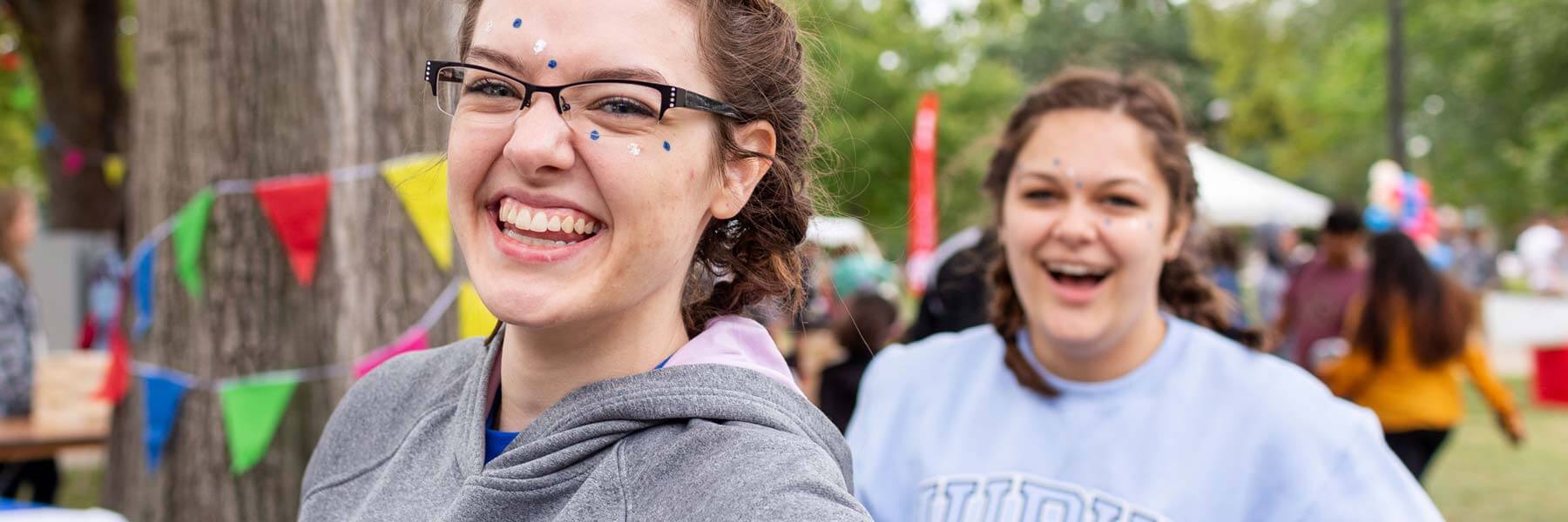 Two students wear face paint and smile during a student event outside.